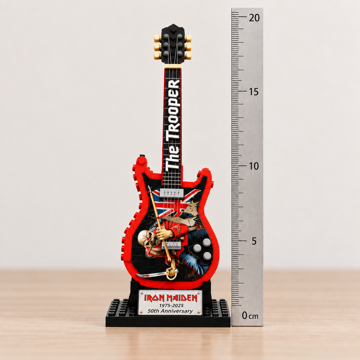 Miniatura da guitarra Iron Maiden The Trooper ao lado de uma régua em centímetros, mostrando as dimensões aproximadas de 19,5 × 6,5 × 10 cm.